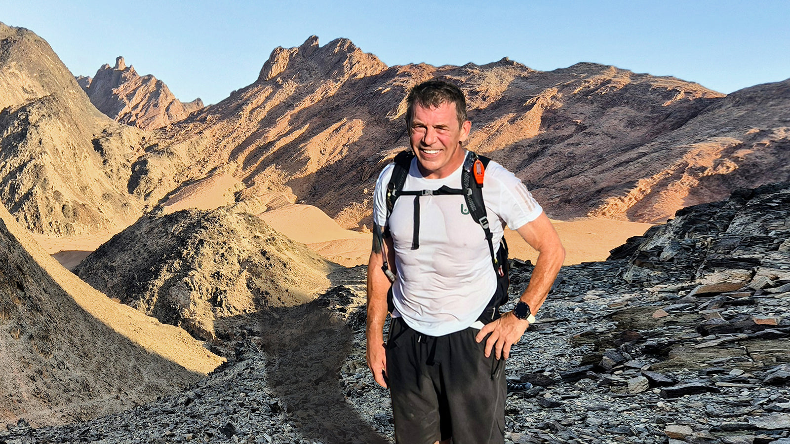 Uthfullife man with hiking gear standing in a desert landscape with mountains.